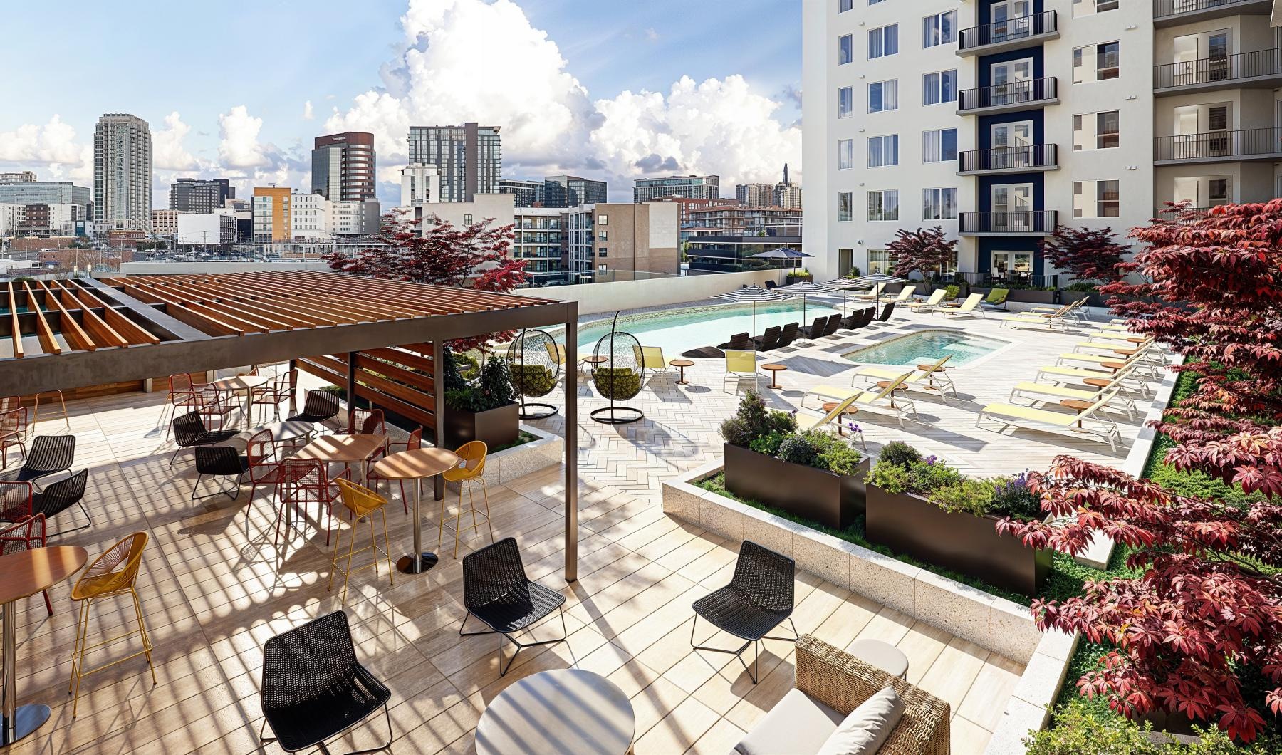 a deck with chairs and tables and plants on it with buildings in the background